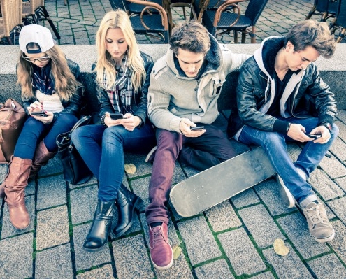 Bild zeigt Gruppe Jugendlicher mit Handy auf der Straße sitzend