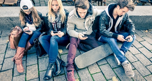 Bild zeigt Gruppe Jugendlicher mit Handy auf der Straße sitzend